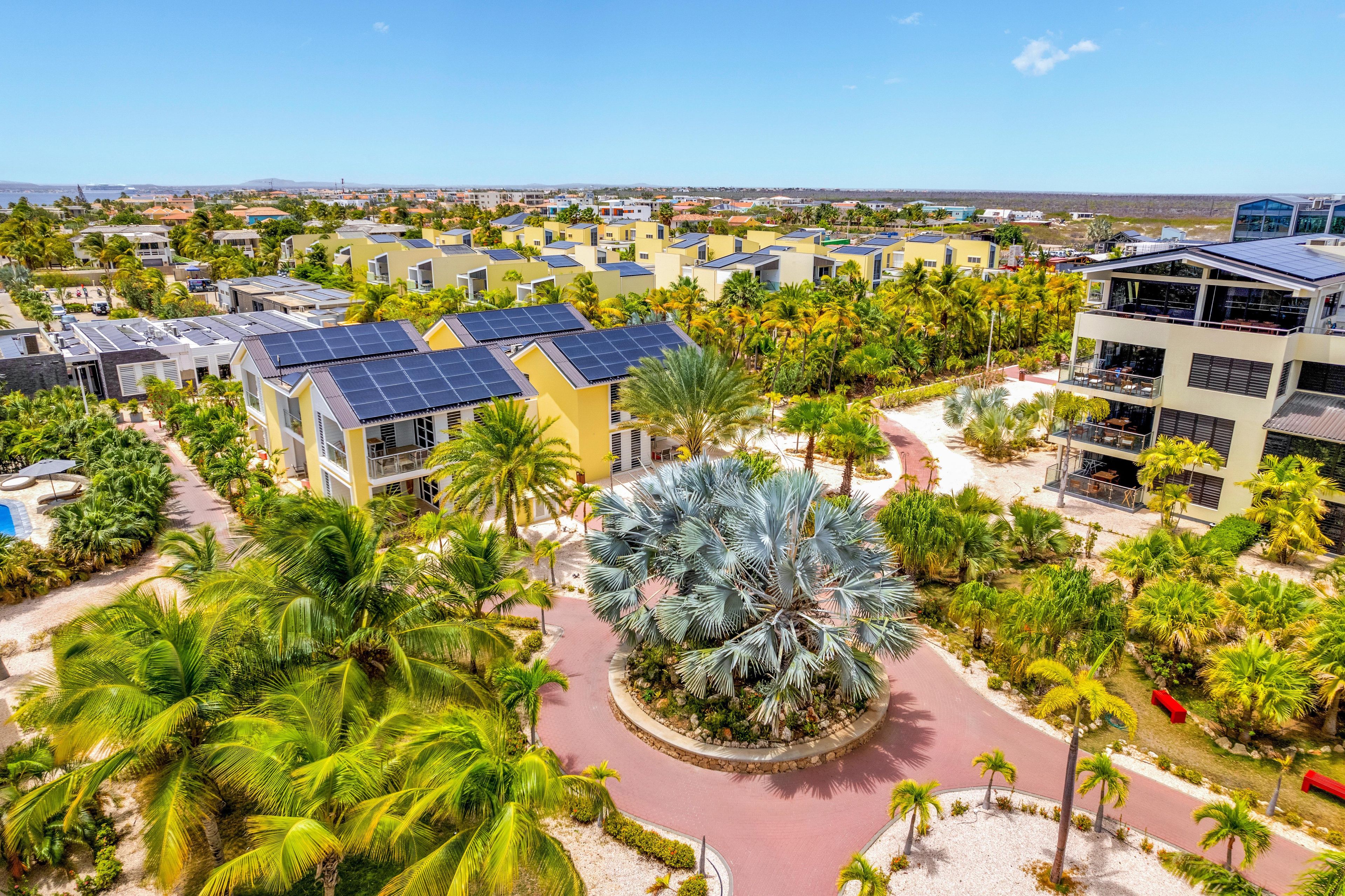 A resort with multiple buildings, solar panels, and a central landscaped area with palm trees.