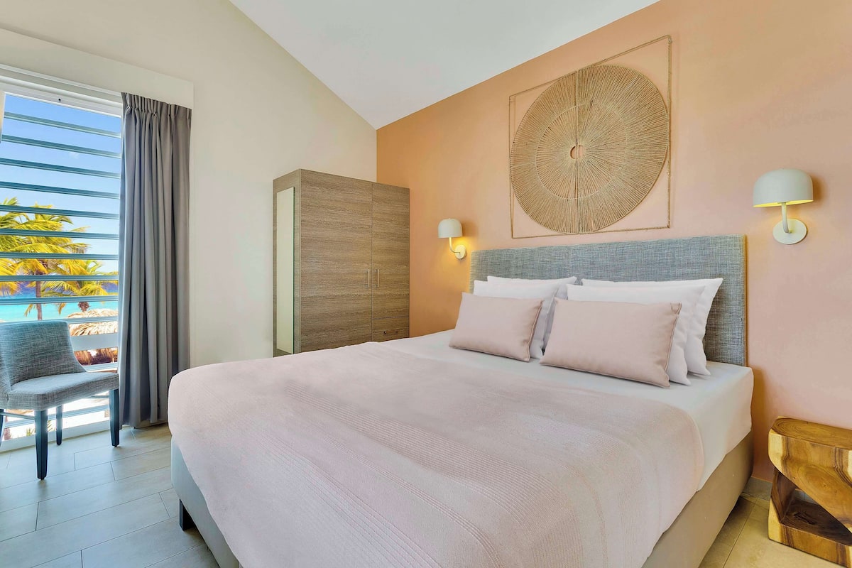 Een slaapkamer met een bed, een stoel, een kledingkast en een wandlamp.