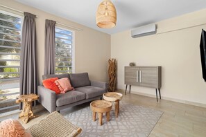 A modern living room with a grey sofa, a wooden coffee table, a woven chair, and a cabinet with a flat-screen TV.