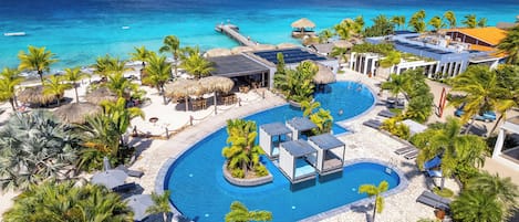 Un complexe hôtelier doté d’une grande piscine, de palmiers et offrant une vue sur l’océan.