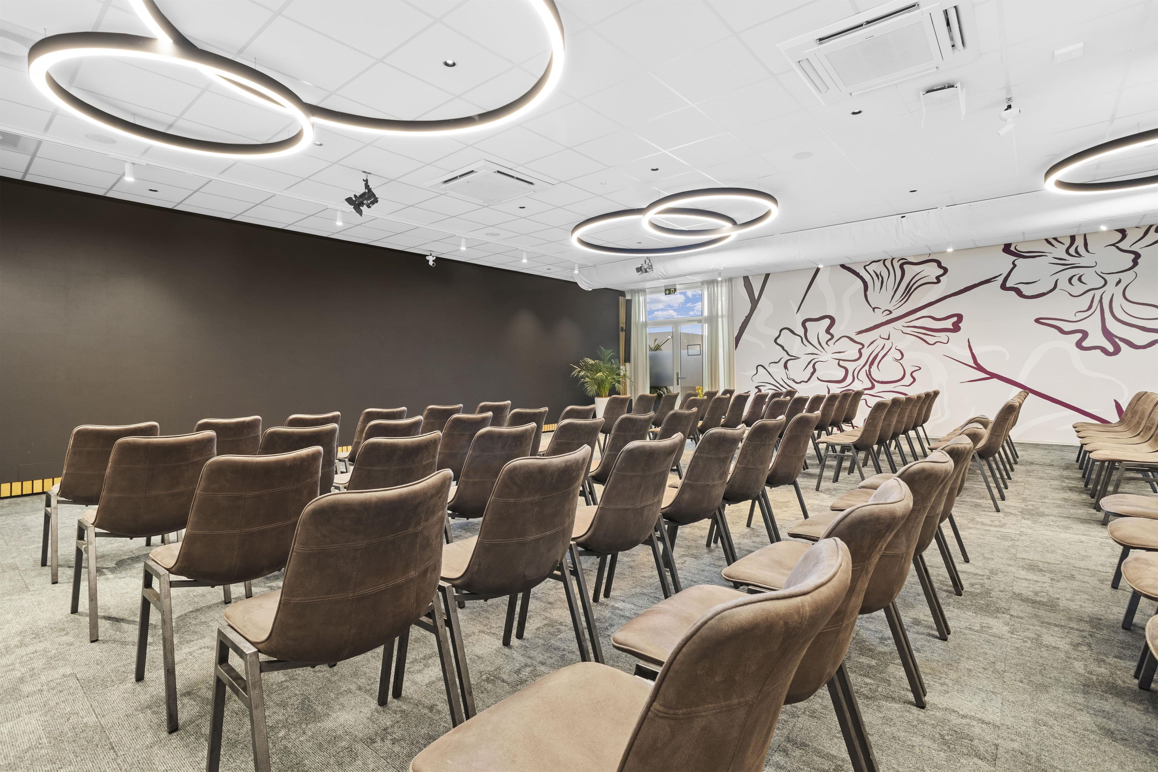 A conference room with rows of chairs, a patterned wall, and ceiling lights.