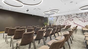 A conference room with rows of chairs, a patterned wall, and ceiling lights.