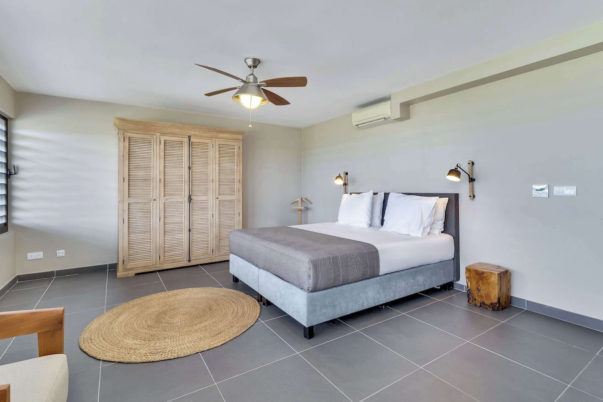 A bedroom with a bed, a ceiling fan, a wooden wardrobe, a bedside table, and a floor lamp.