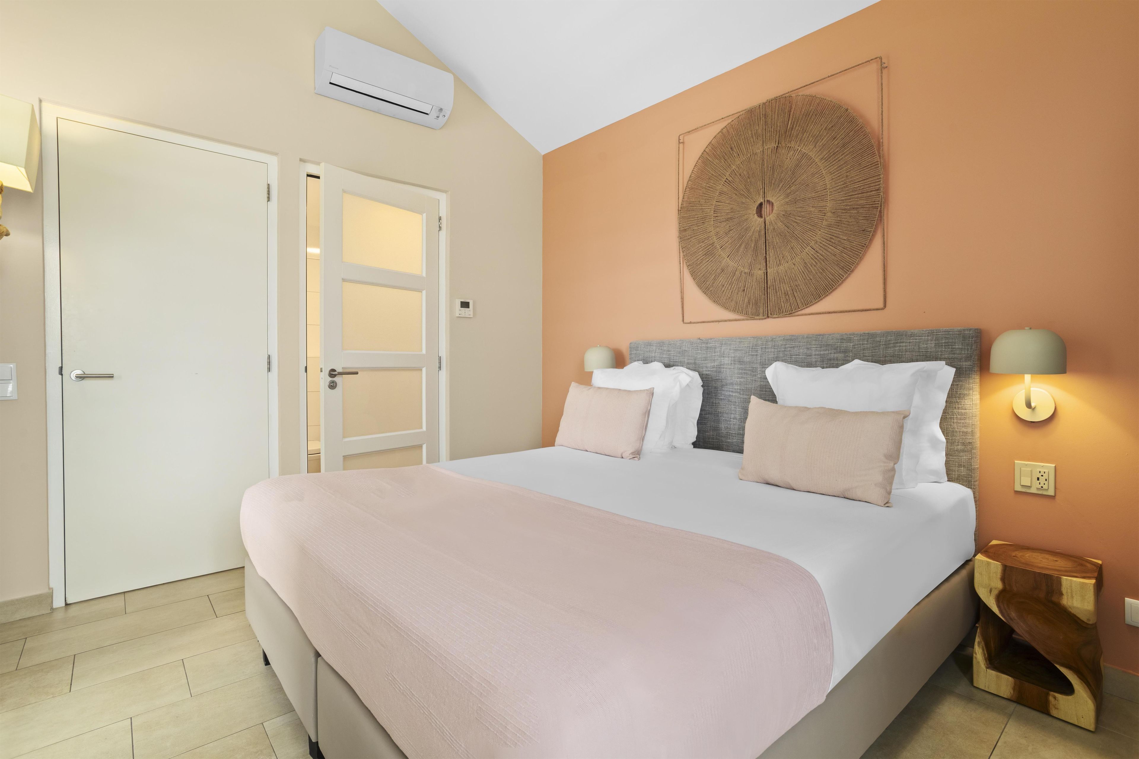 A bedroom with a bed, bedside lamps, a wall-mounted air conditioner, and a door.