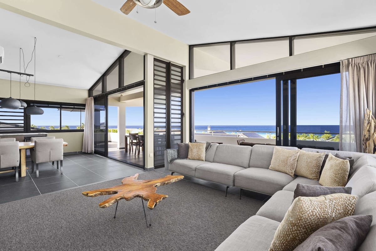 A modern living room with a large sectional sofa, a wooden coffee table, and a view of the ocean.