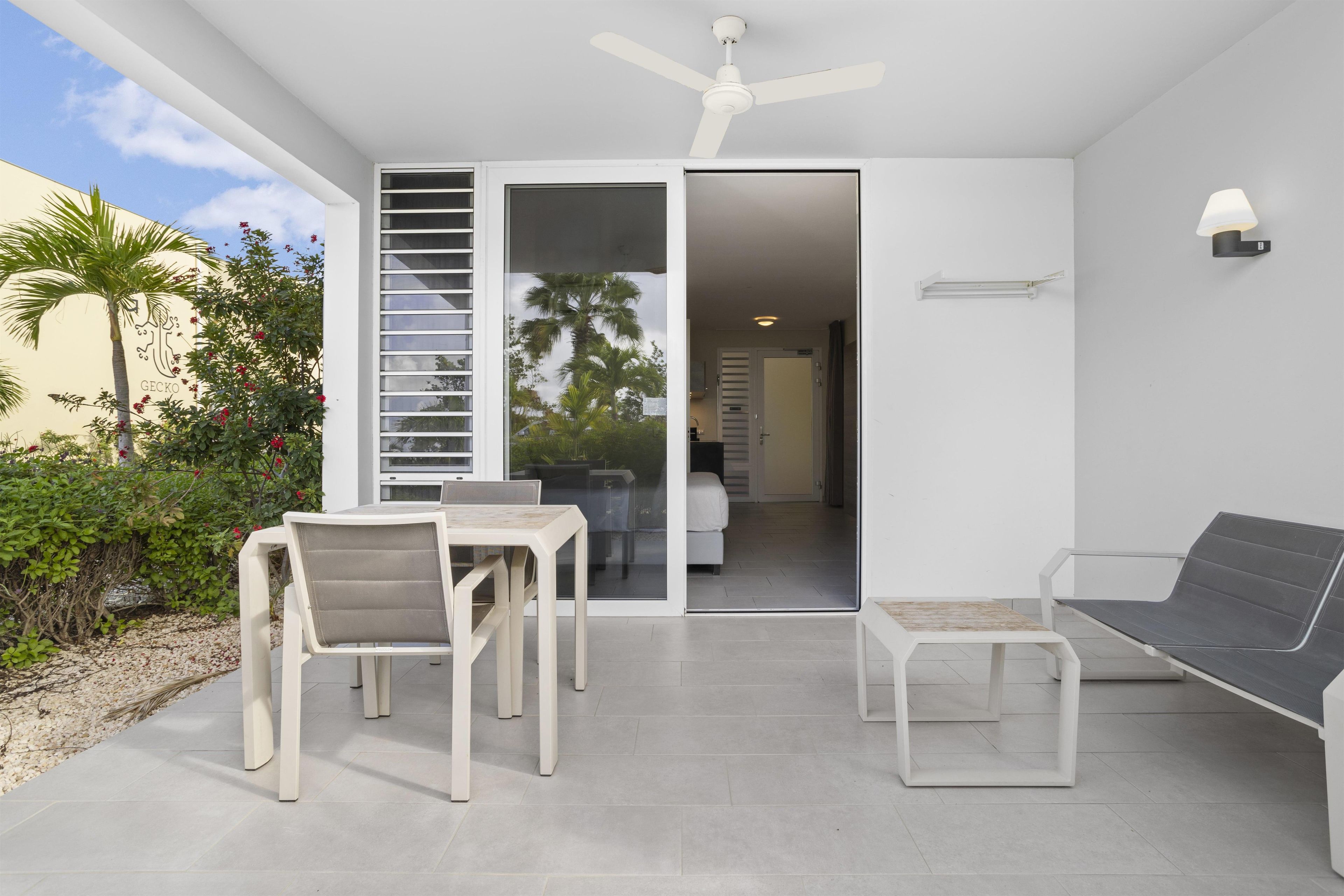 A modern outdoor patio with a dining table and chairs, a lounge chair, and a ceiling fan.