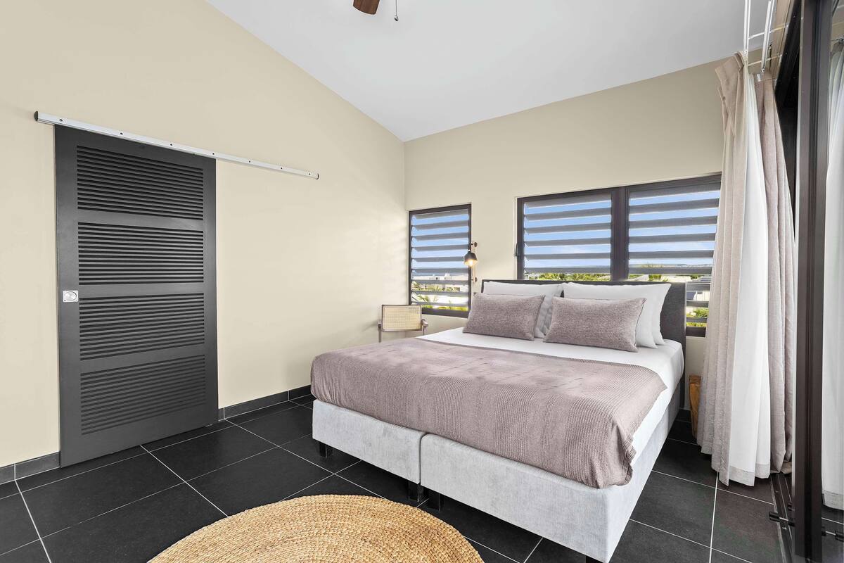 A bedroom with a bed, two windows, a ceiling fan, and a view of the outdoors.