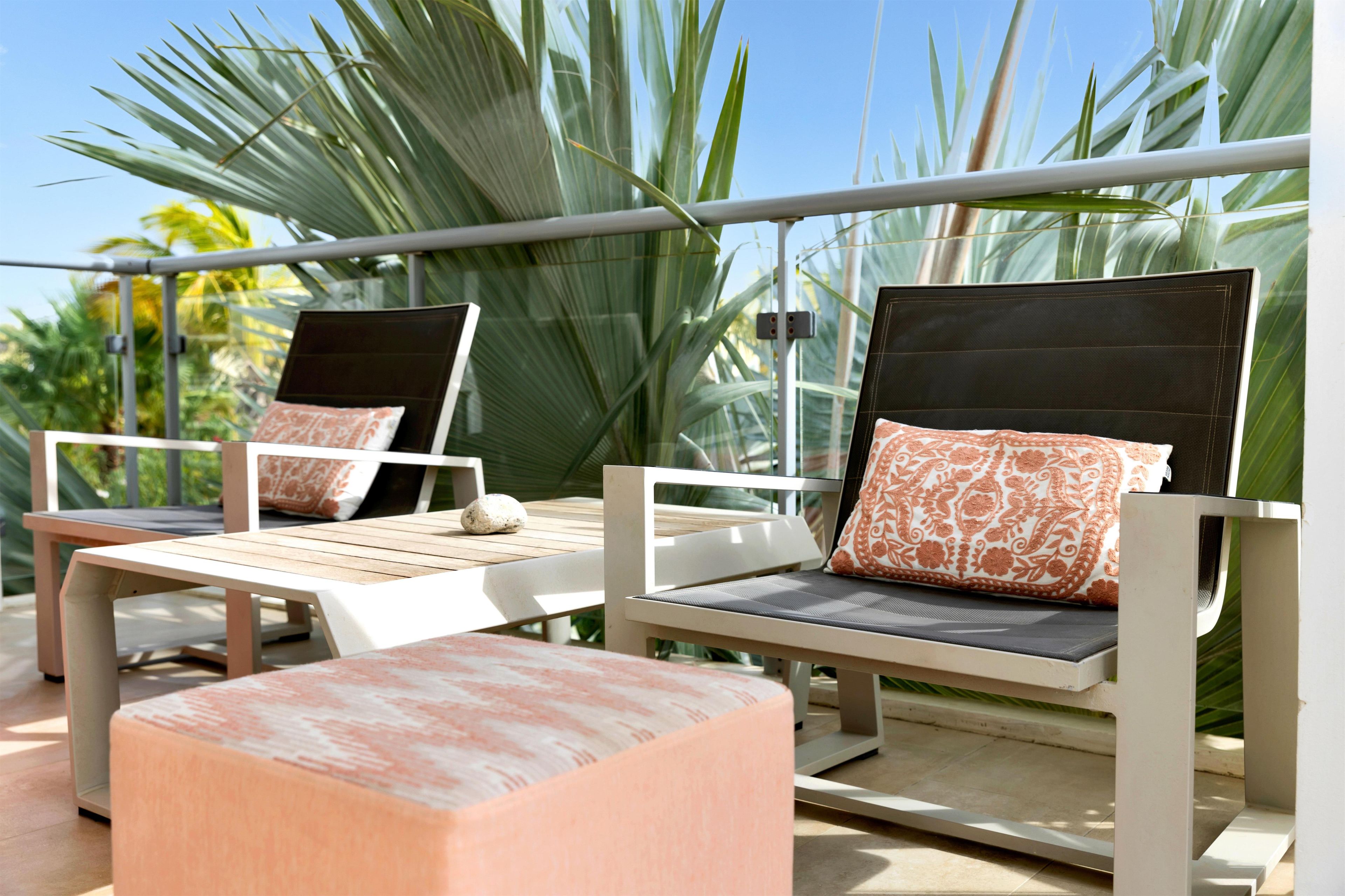 Two lounge chairs with cushions, a small table, and a view of palm trees.