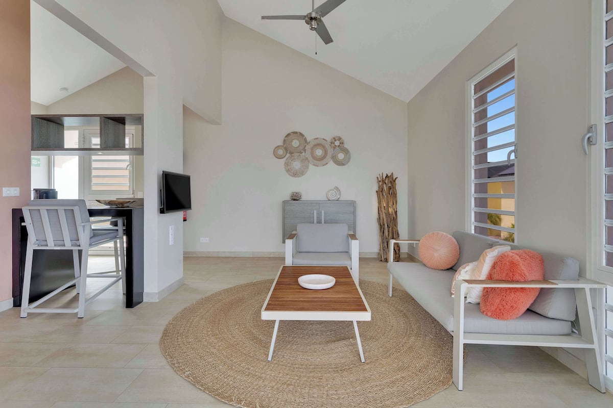 A modern living room with a dining area, a sofa with cushions, a coffee table, and a TV.