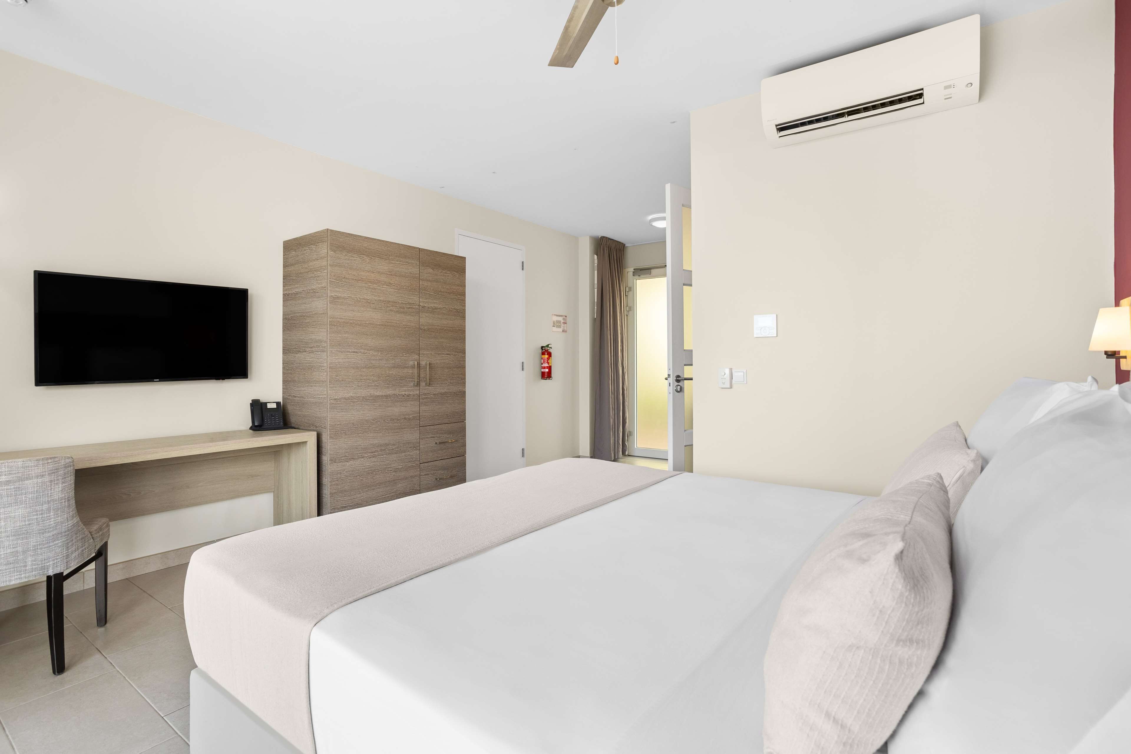 A hotel room with a bed, a desk, a television, and an air conditioning unit.