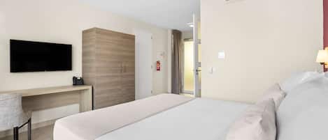 Una habitación de hotel con cama, escritorio, televisor y aire acondicionado.