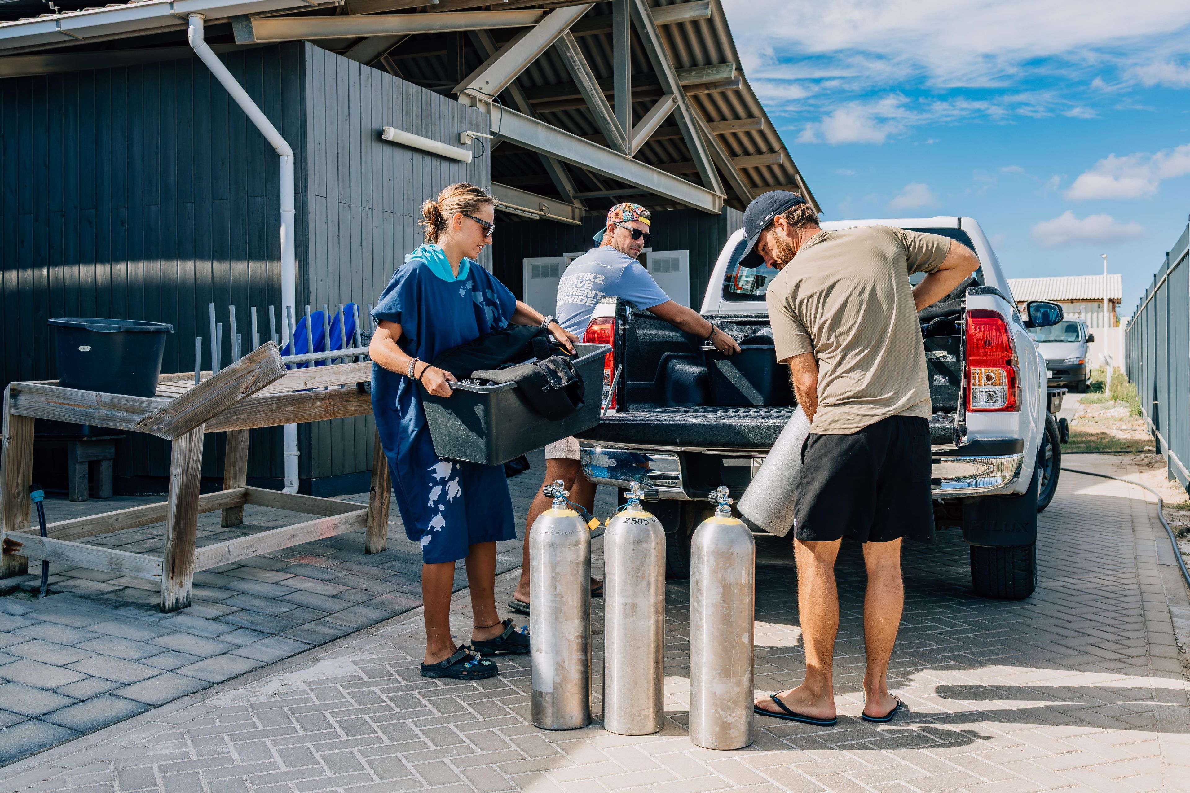 A group of people loading large metal cylinders into the back of a pickup truck.