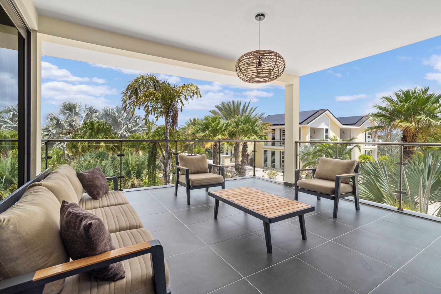 Un balcón con sofá, sillas y una mesa, con vistas a una zona residencial con palmeras y casas.