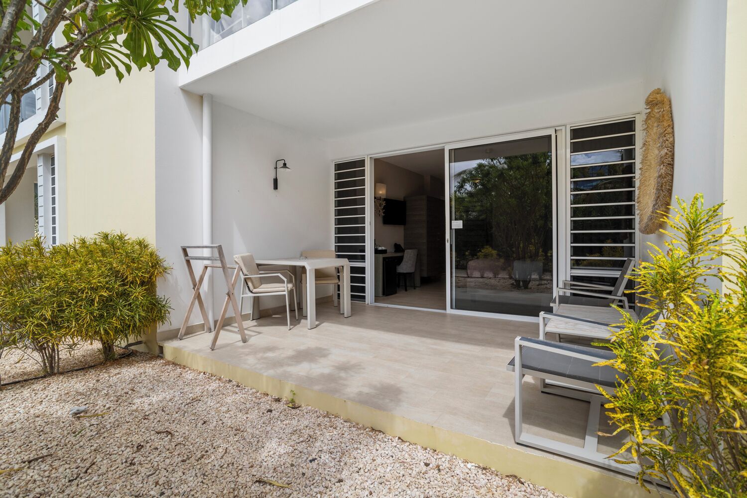 A modern outdoor patio with a table and chairs, a small garden area, and a sliding glass door leading to an interior space.