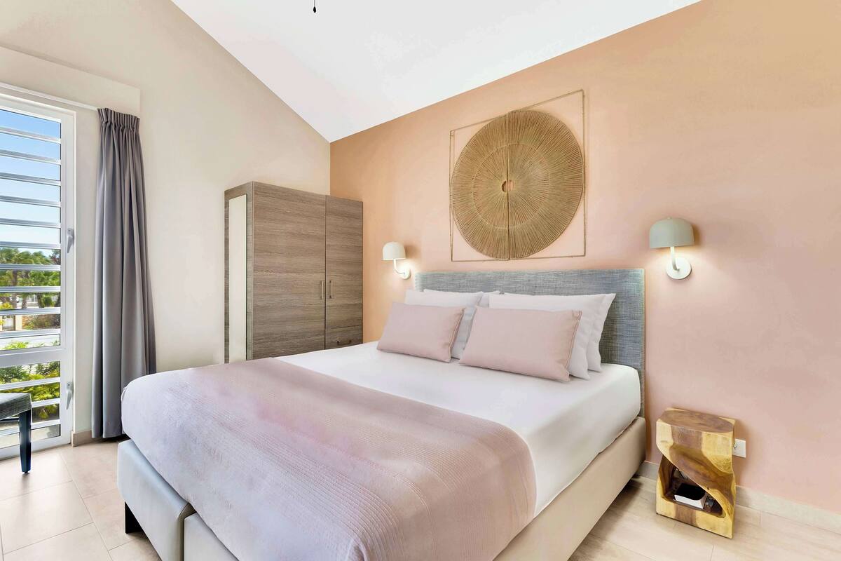 A bedroom with a bed, a wardrobe, a wall-mounted lamp, and a view through a window.