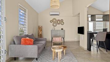 A modern living room with a grey sofa, a coffee table, and a dining area with a TV and chairs.