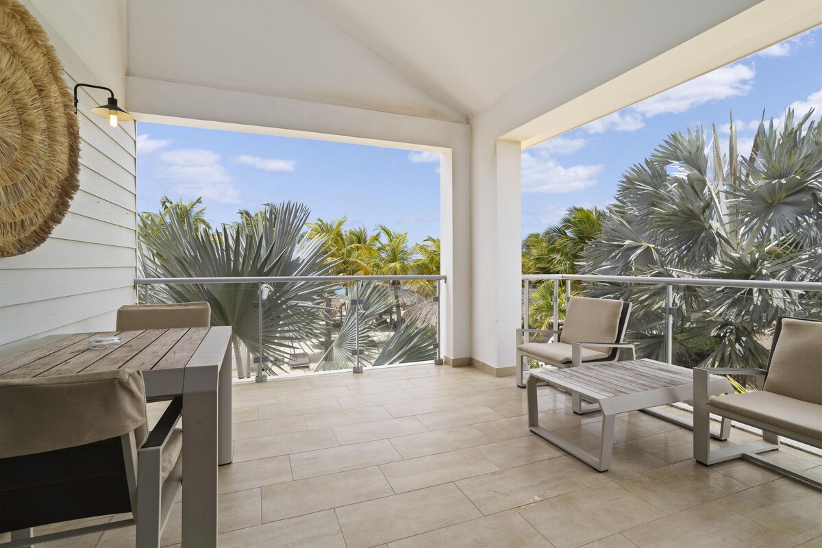 A balcony with a table and chairs, overlooking palm trees and a clear sky.