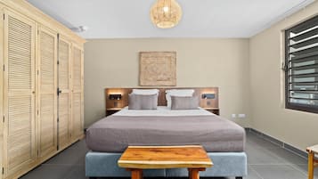 Een slaapkamer met een bed, nachtkastjes, een kledingkast, een hanglamp en een raam met jaloezieën.