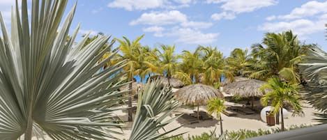 A tropical resort with palm trees, thatched umbrellas, and sun loungers on a sandy beach.