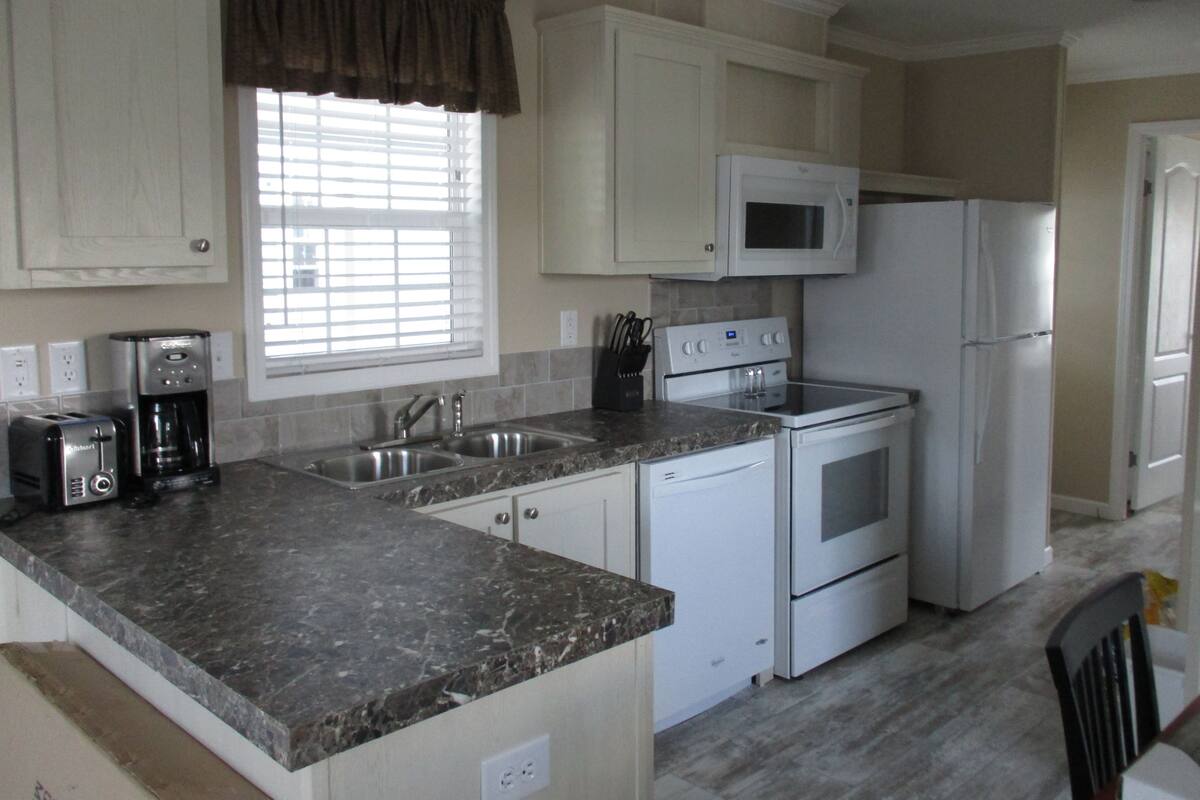 A kitchen with white cabinets, a granite countertop, a microwave, a refrigerator, a stove, and a coffee maker.