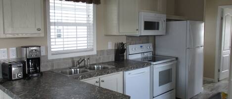 A kitchen with white cabinets, a granite countertop, a microwave, a refrigerator, a stove, and a coffee maker.