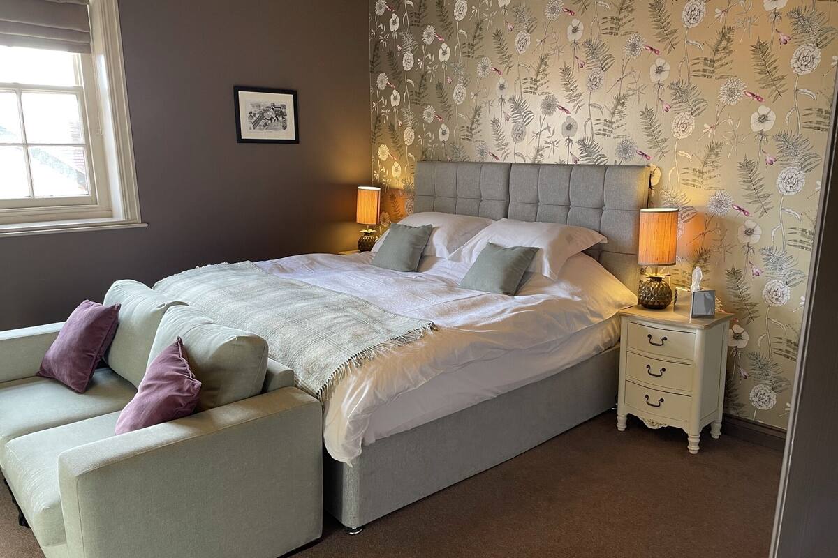 Ein Schlafzimmer mit einem Bett, zwei Nachttischen, einem Sessel und einem Fenster.