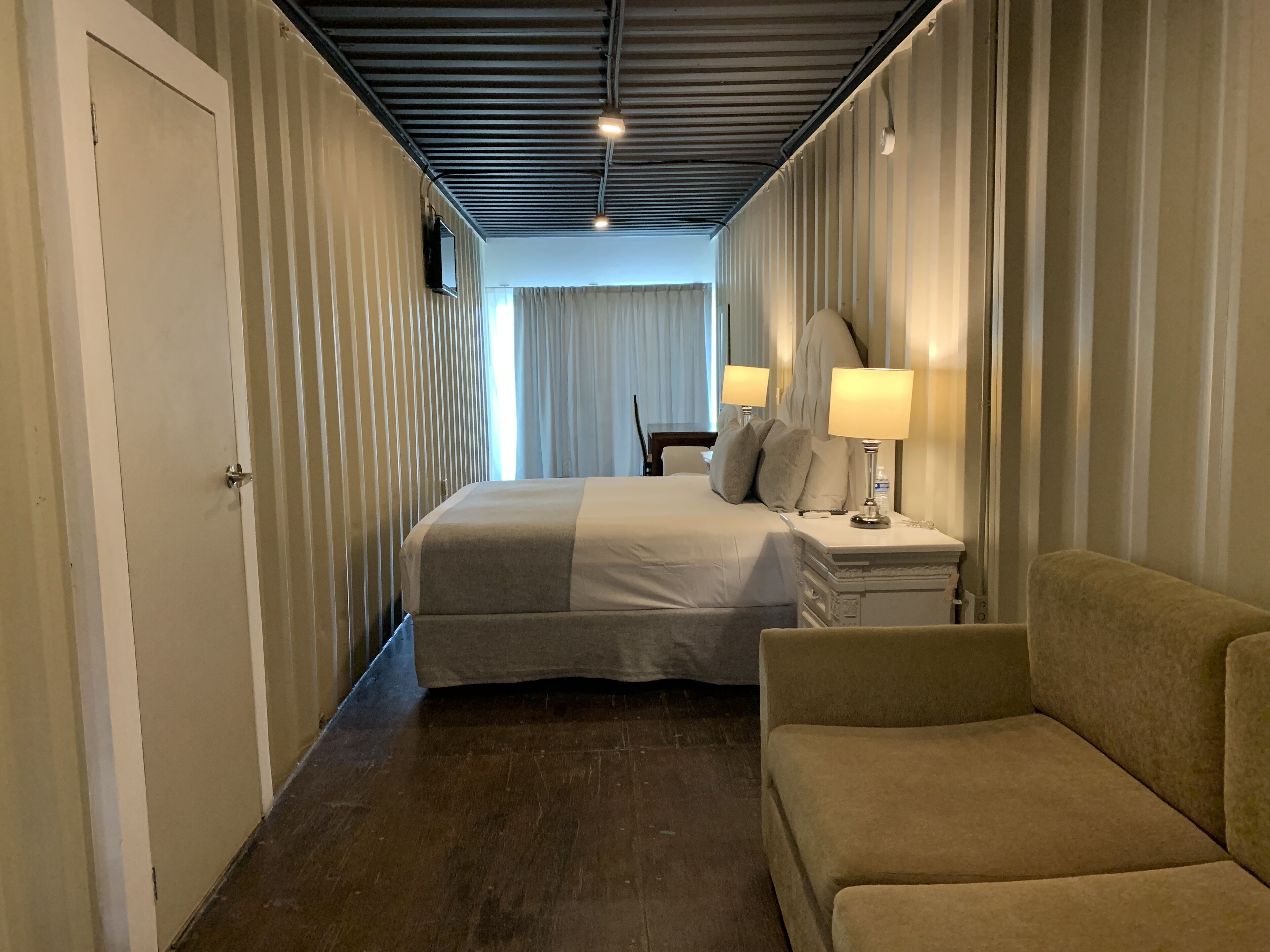 A hotel room with a bed, bedside lamps, a nightstand, a sofa, and a window with curtains.
