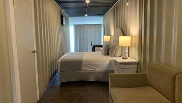 A hotel room with a bed, bedside lamps, a nightstand, a sofa, and a window with curtains.