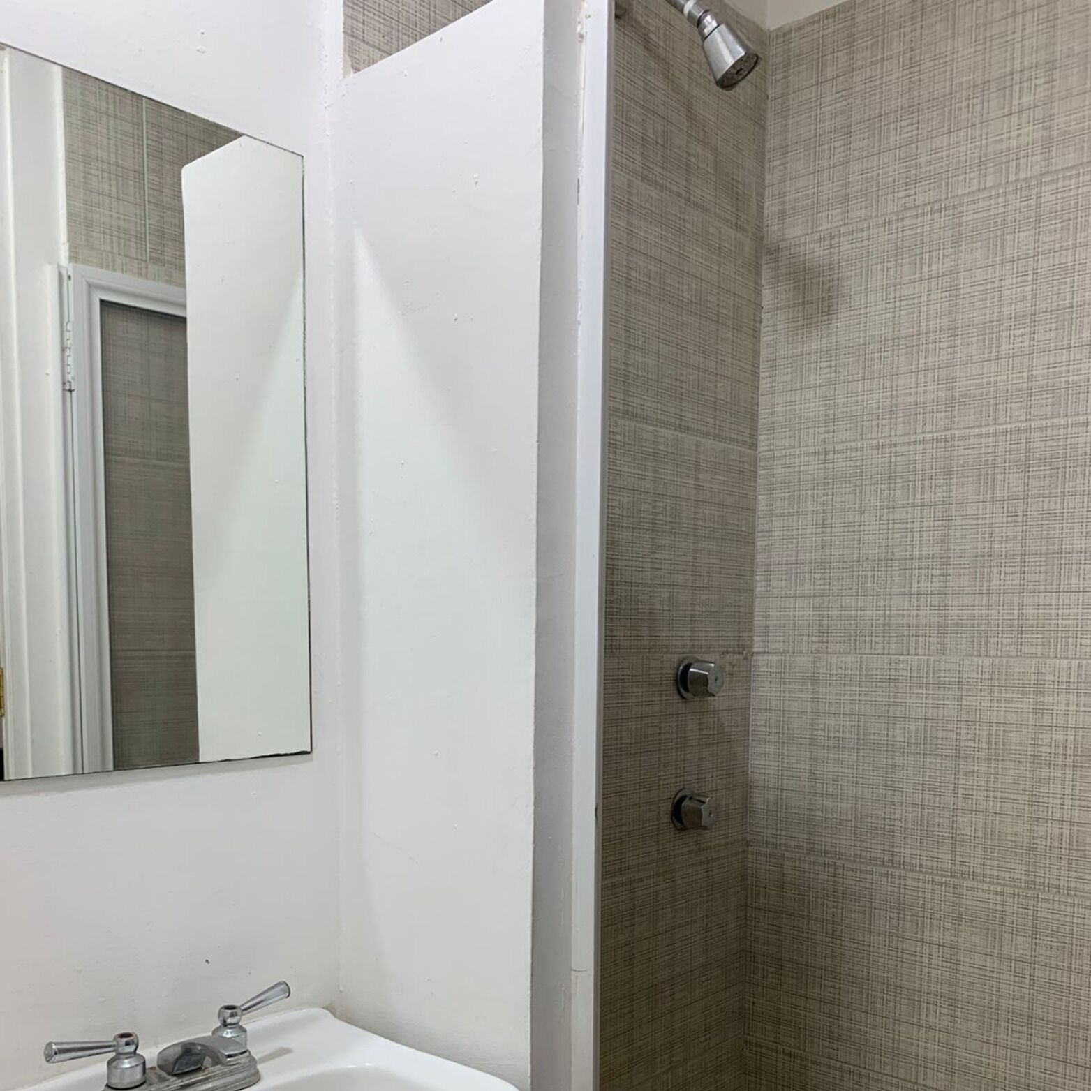 A bathroom with a white sink, a mirror, and a shower with a textured wall.