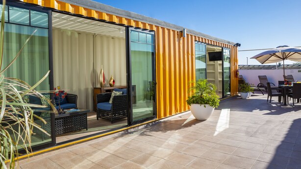 A modern building with large glass doors, outdoor seating, and potted plants. - Container Inn Hotel Aeropuerto (Puerto Vallarta)