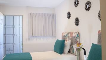 A bedroom with a bed, a desk, and a window with curtains.