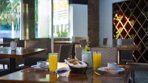 A breakfast setting with a table set for two, including plates, cups, a basket of bread, and two glasses of orange juice. - Container Inn Hotel Aeropuerto (Puerto Vallarta)