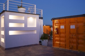 A modern building with illuminated rectangular cutouts on the facade, a staircase leading to an upper level, and a large container-like structure with signage.