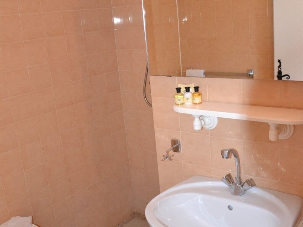 A bathroom with a white sink, a mirror, and a shelf with toiletries.