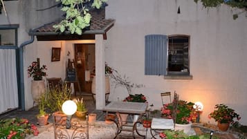 Ein gemütlicher Sitzbereich im Freien mit Tisch und Stühlen, umgeben von Kübelpflanzen und einem kleinen Garten.