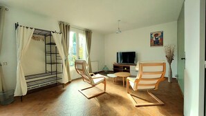 Una habitación con literas, dos sillas de madera, una mesita, un televisor y un cuadro en la pared.