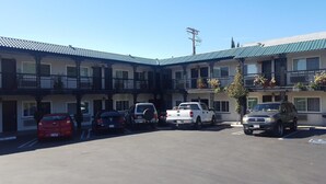 A motel with a central courtyard parking area, multiple balconies with potted plants, and a clear blue sky. - Welcome Inn on Colorado Blvd (Los Angeles)