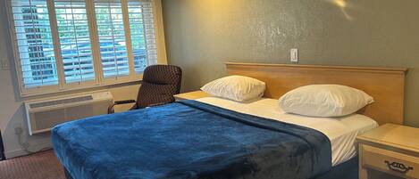 Un dormitorio con una cama grande, una silla, una mesita de noche y una ventana con persianas.