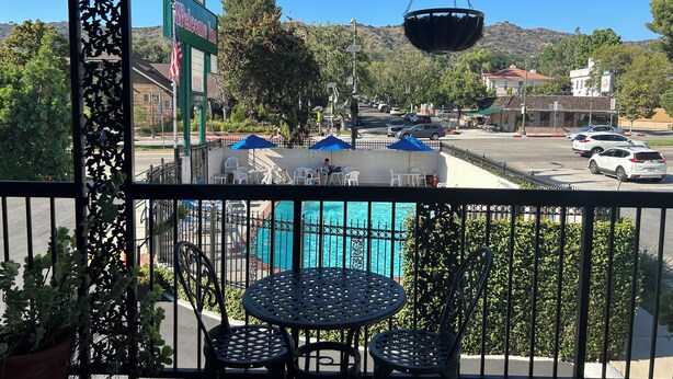 A balcony with a view of a swimming pool, a 'Welcome Inn' sign, and a parking area with cars. - Welcome Inn on Colorado Blvd (Los Angeles)