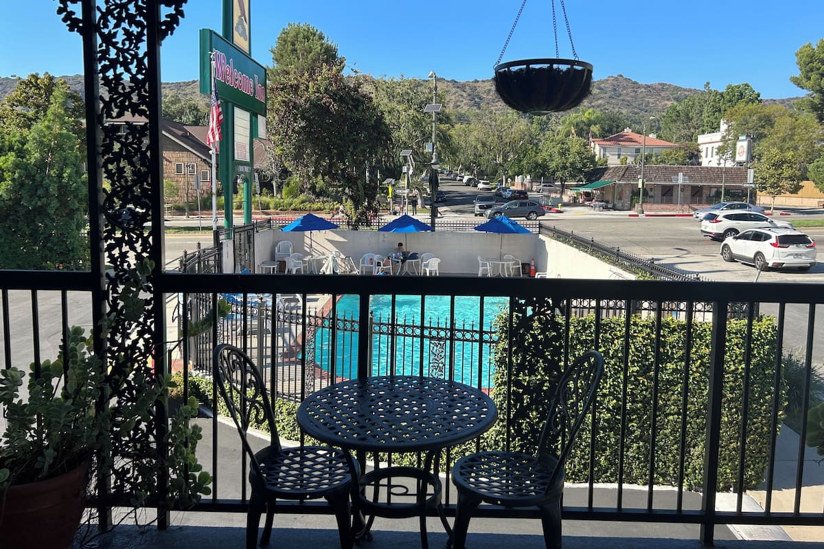 A balcony with a view of a swimming pool, a 'Welcome Inn' sign, and a parking area with cars.