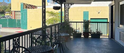 A covered outdoor area with metal chairs and tables, potted plants, and a green gate.