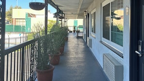 A covered corridor with potted plants, a metal railing, and a door with a number sign. - Welcome Inn on Colorado Blvd (Los Angeles)