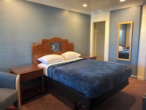 Een keurig opgeruimde hotelkamer met een eenpersoonsbed, een nachtkastje, een stoel en een spiegel aan de muur.