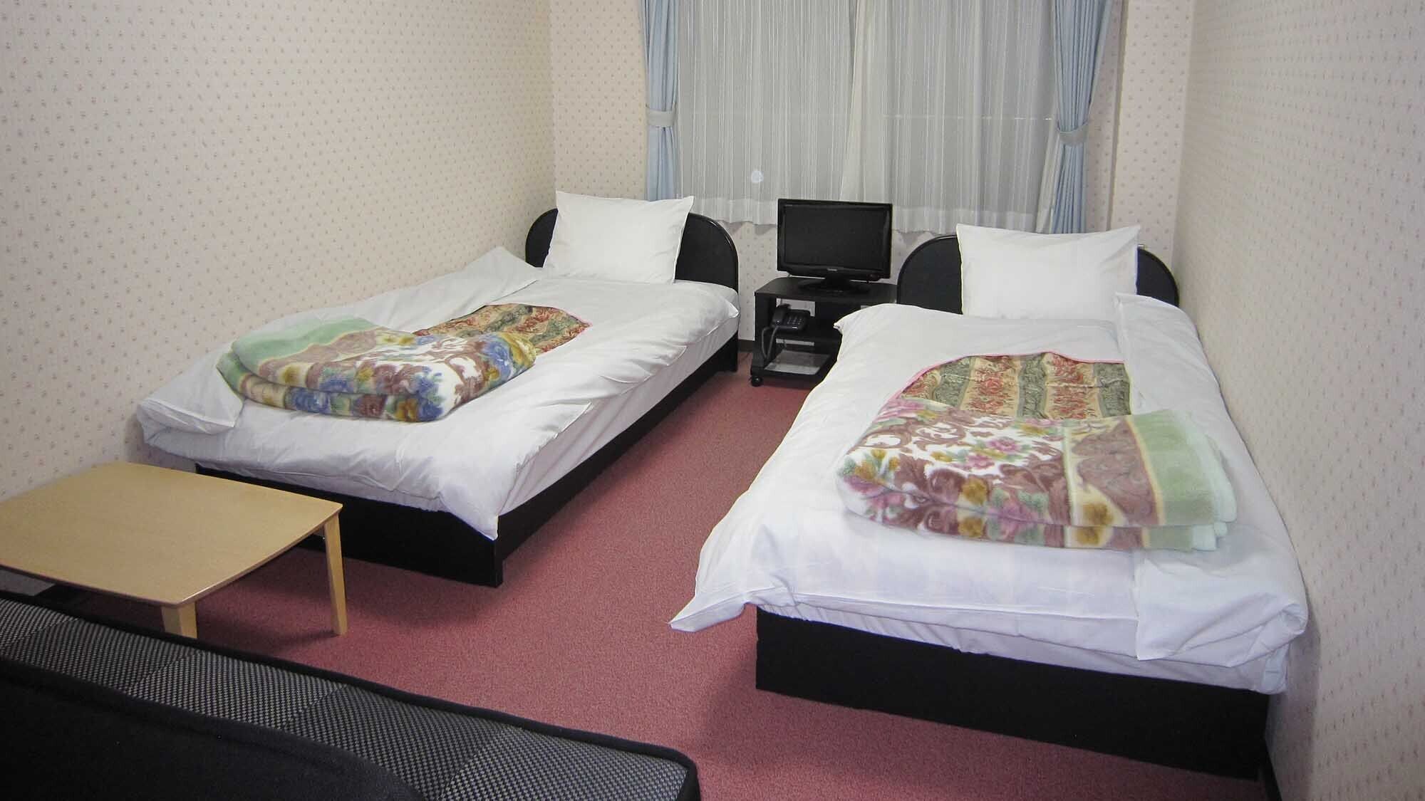Een hotelkamer met twee enkele bedden, een tafeltje, een televisie en een raam met gordijnen.
