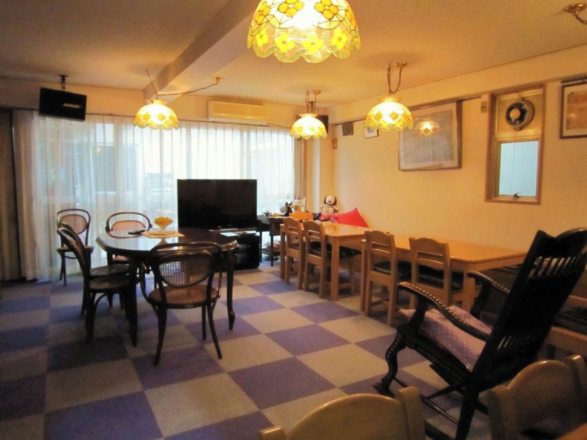 Een woonkamer met een zwart-wit schakeerd vloer, een eettafel, stoelen, een televisie en decoratieve lampen.