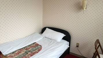 A single bed with white bedding and a floral-patterned throw, a black headboard, and a wall-mounted light fixture.