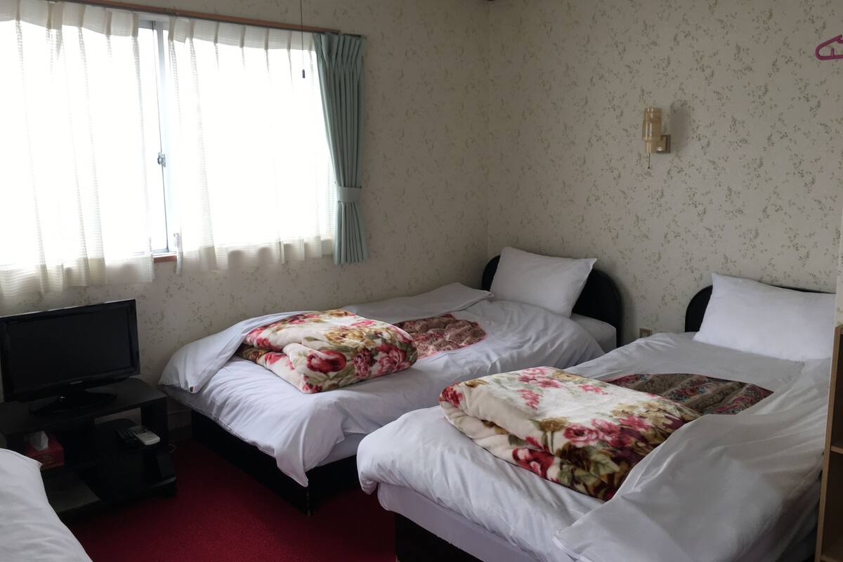 Ein Hotelzimmer mit zwei Betten, einem Fernseher und einem Fenster mit Vorhängen.