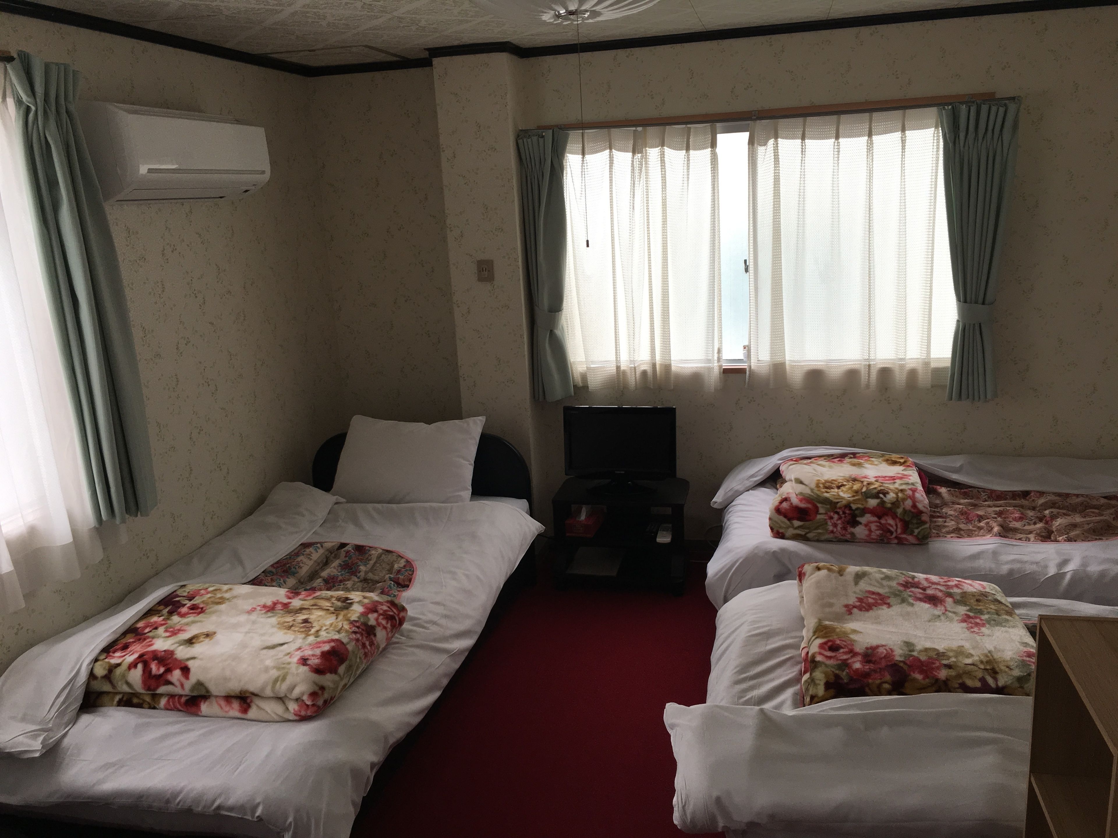A hotel room with two single beds, a TV, and an air conditioning unit.