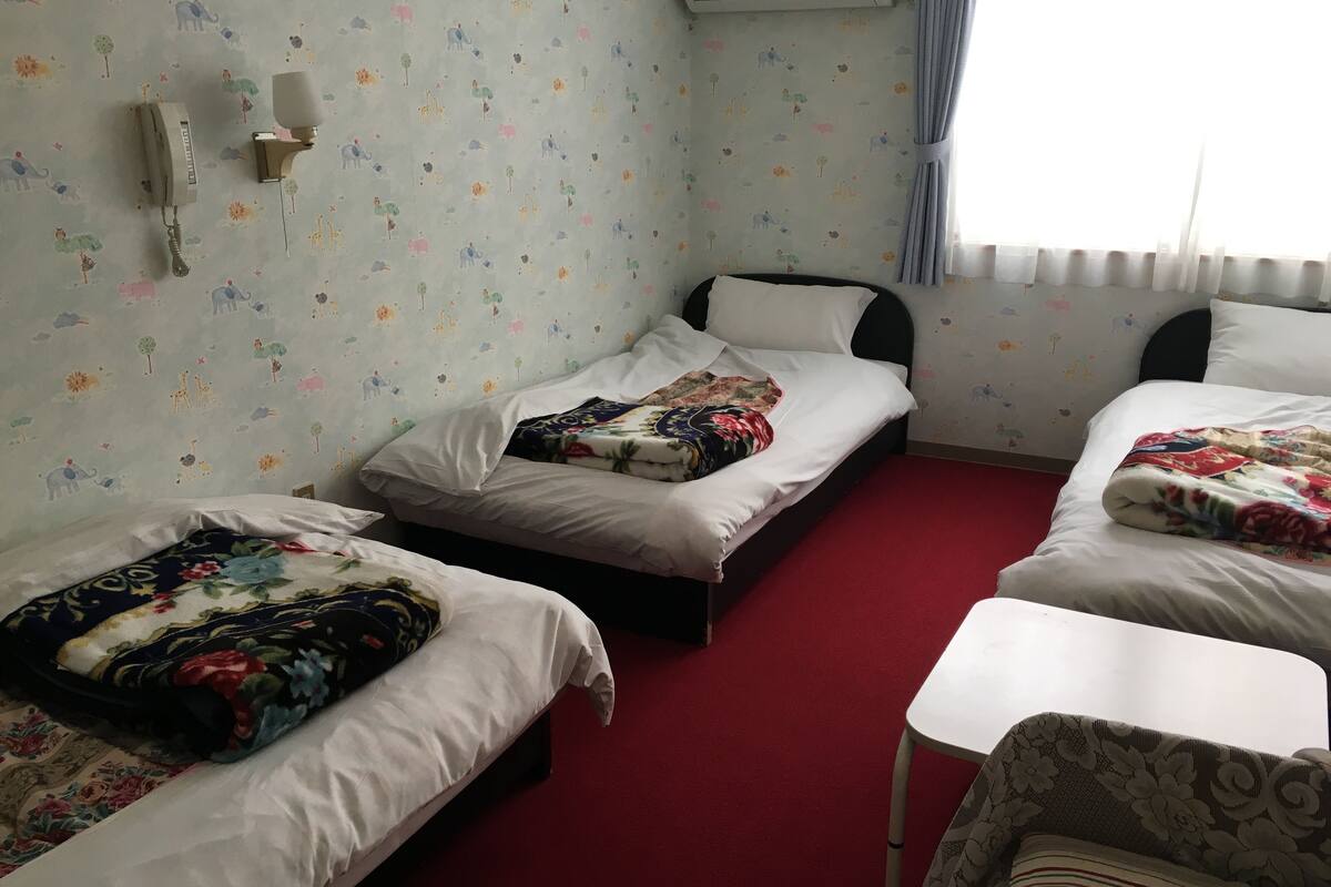 Ein Hotelzimmer mit drei Betten, einem weißen Tisch und einem roten Teppich.