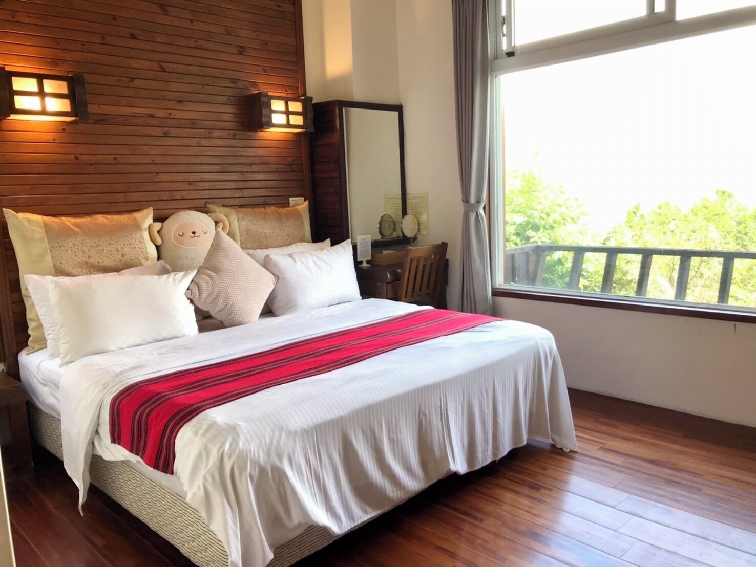 A neatly made bed with a red and white striped blanket, wooden headboard, and two wall-mounted lights.